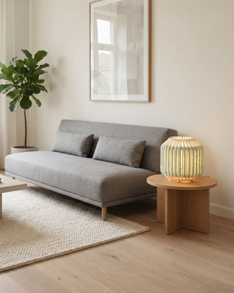 Lampe de table Nukumori allumée sur une table d'appoint en bois, dans un salon lumineux
