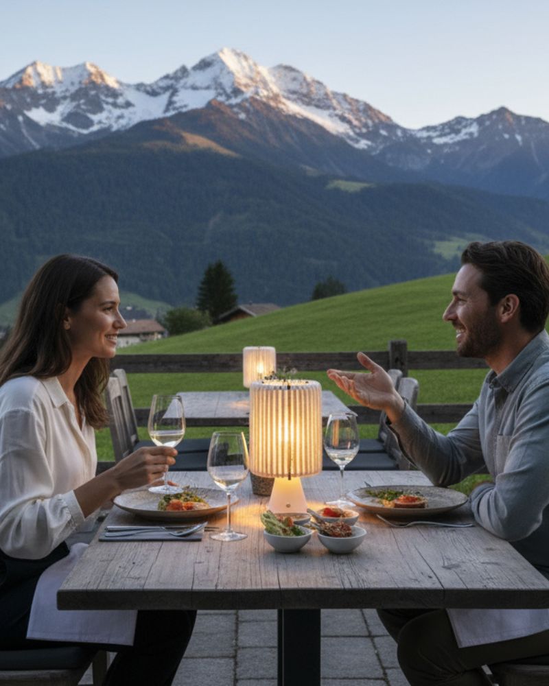 Lampe sans fil Nukumori allumée sur une table en terrasse, face aux montagnes